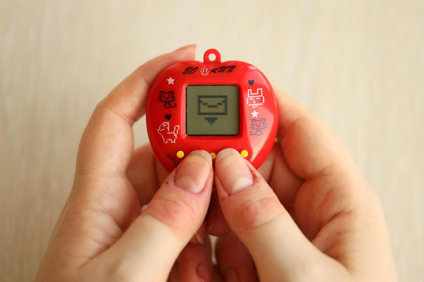 KYIV, UKRAINE - MARCH 9, 2024 Retro pet keychain game tamagotchi in red plastic case in female hands photo