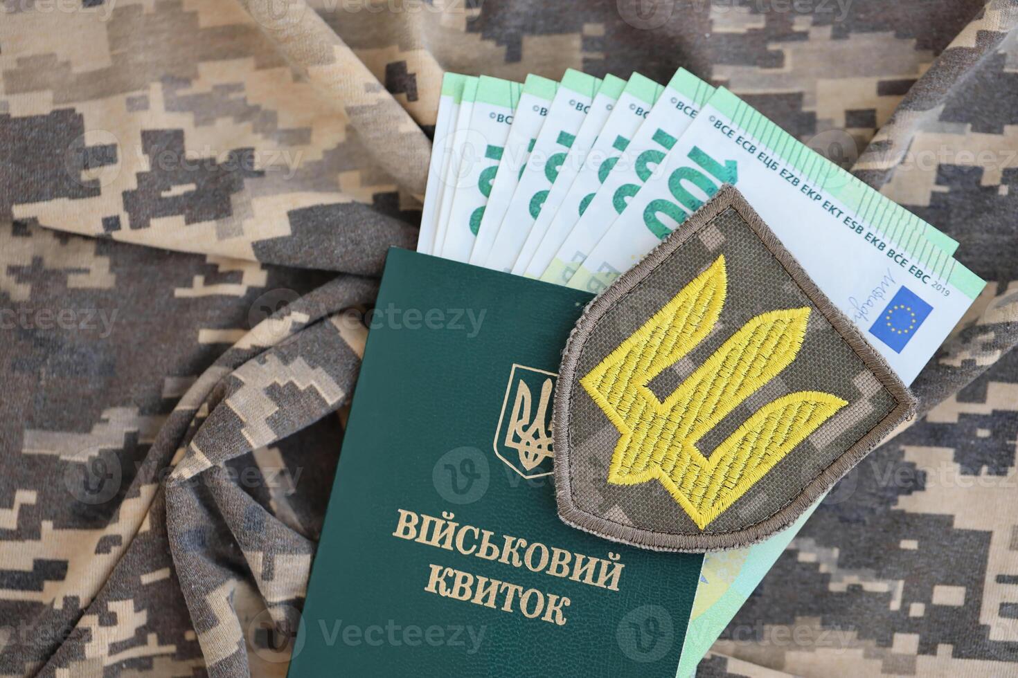 Symbol of Ukrainian army and military ID with bunch of money on the camouflage uniform of a Ukrainian soldier. Concept of payment to military personnel or bribe for deferment from service photo