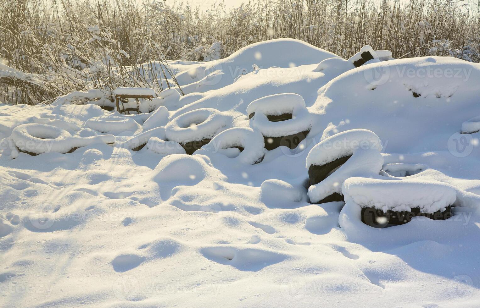 Used and discarded car tires lie on the side of the road, covered with a thick layer of snow photo