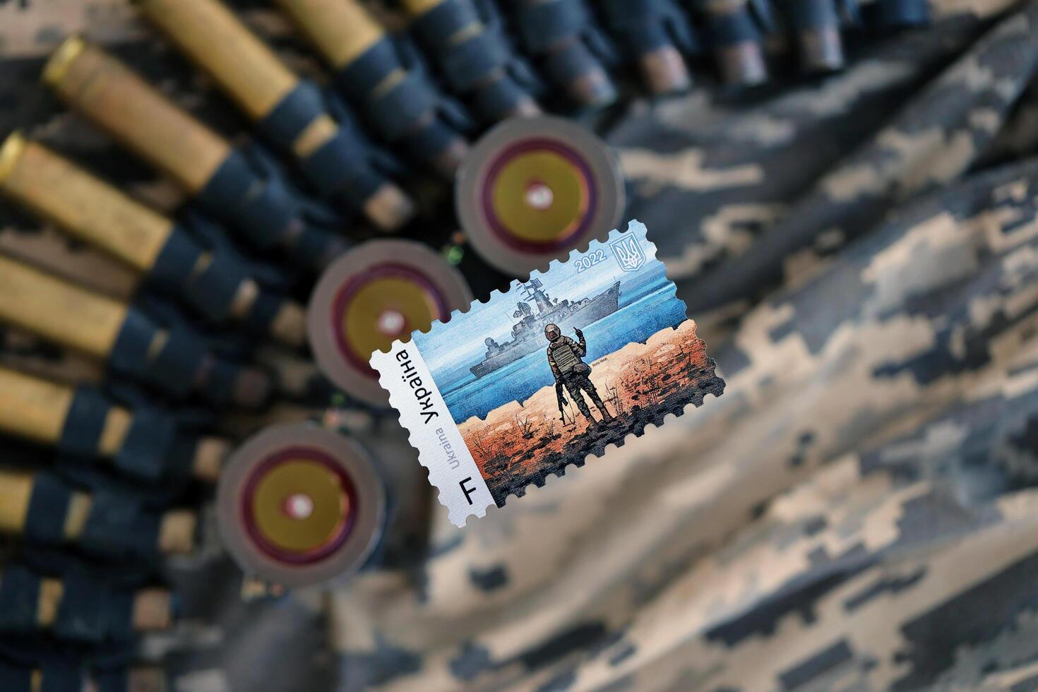 TERNOPIL, UKRAINE - SEPTEMBER 29, 2023 Famous Ukrainian postmark with russian warship and ukrainian soldier as wooden souvenir on army camouflage uniform cloth and machine gun belt photo