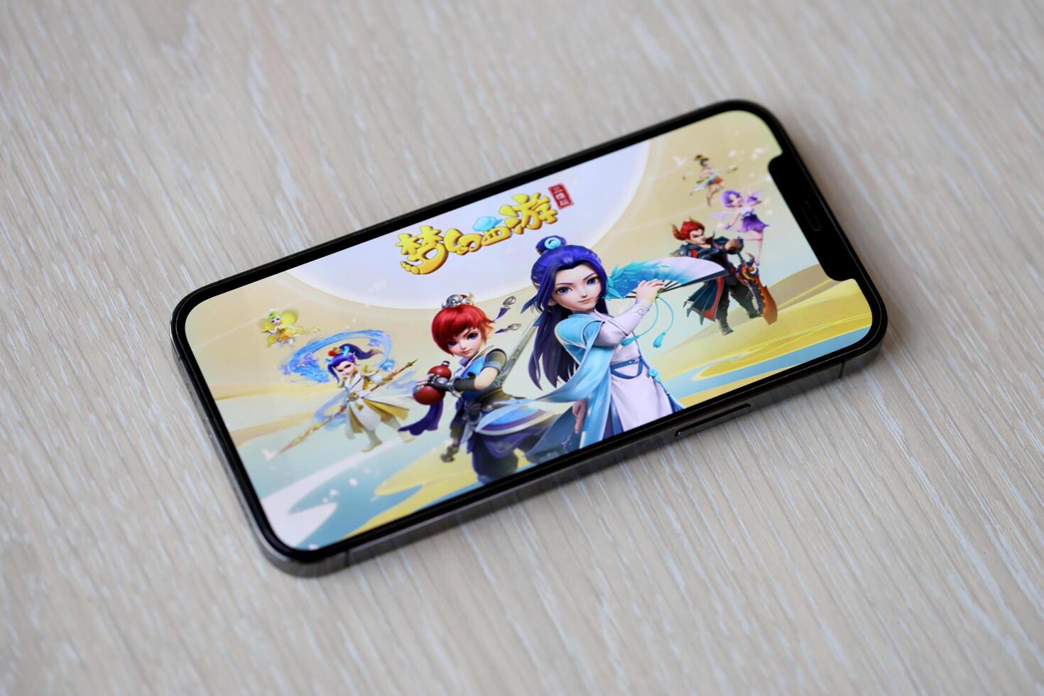 Fantasy Westward Journey mobile iOS game on iPhone 15 smartphone screen on wooden table during mobile gameplay photo