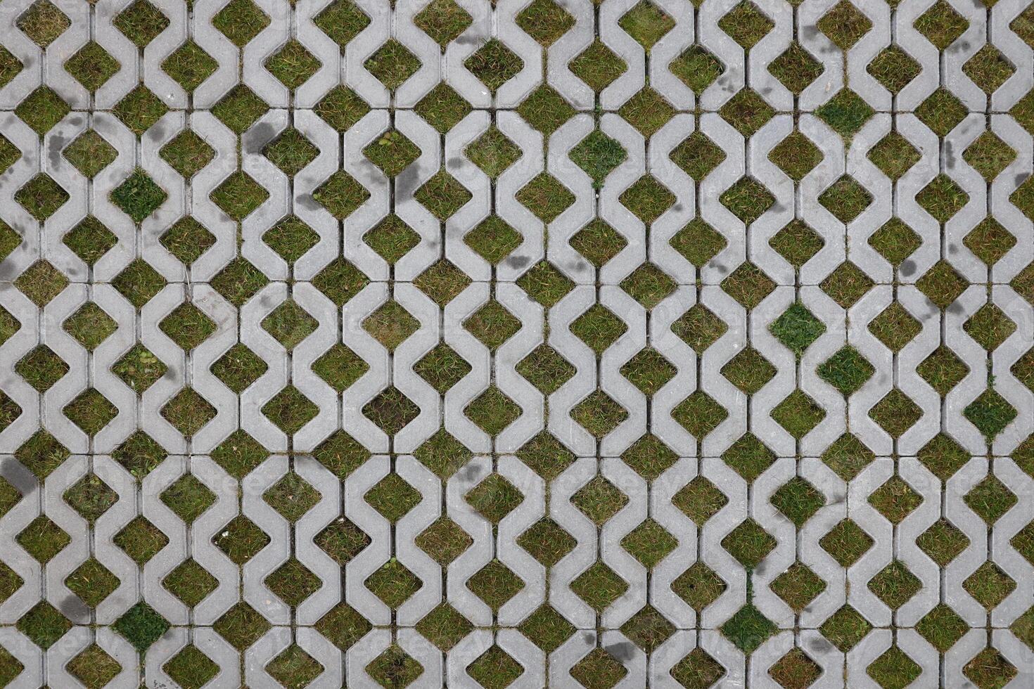 Geometric background of eco floor bricks and green grass. Eco parking texture. Floor stone tile with a rhomb hole for grass. Eco-friendly parking of concrete cells photo
