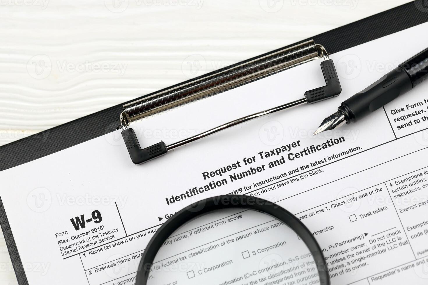 IRS Form W-9 Request for taxpayer identification number and certification blank on A4 tablet lies on office table with pen and magnifying glass photo