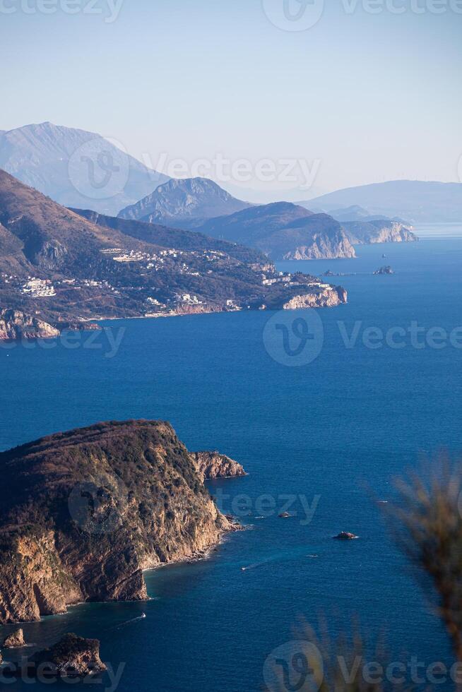 Colorful winter seascape with blue water of the Adriatic Sea and the island of Sveti Nikola near the city of Budva in Montenegro. View from above through the trees. Vertical photo