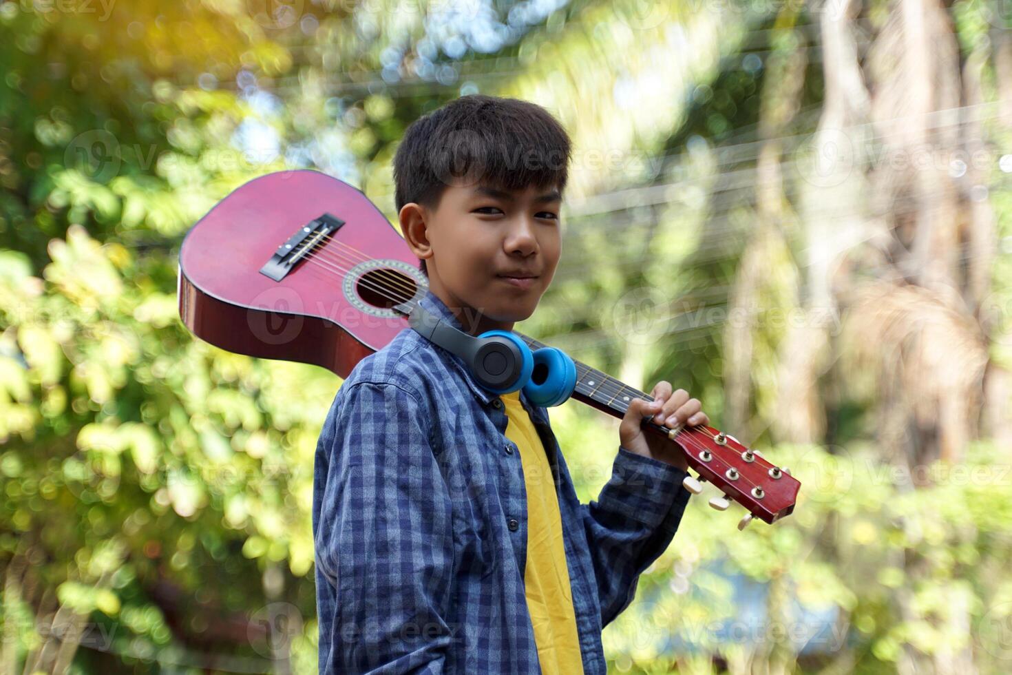 Asian boy carrying Ukulele on his shoulder to play with friends at a summer camp at a national park. Soft and selective focus. photo