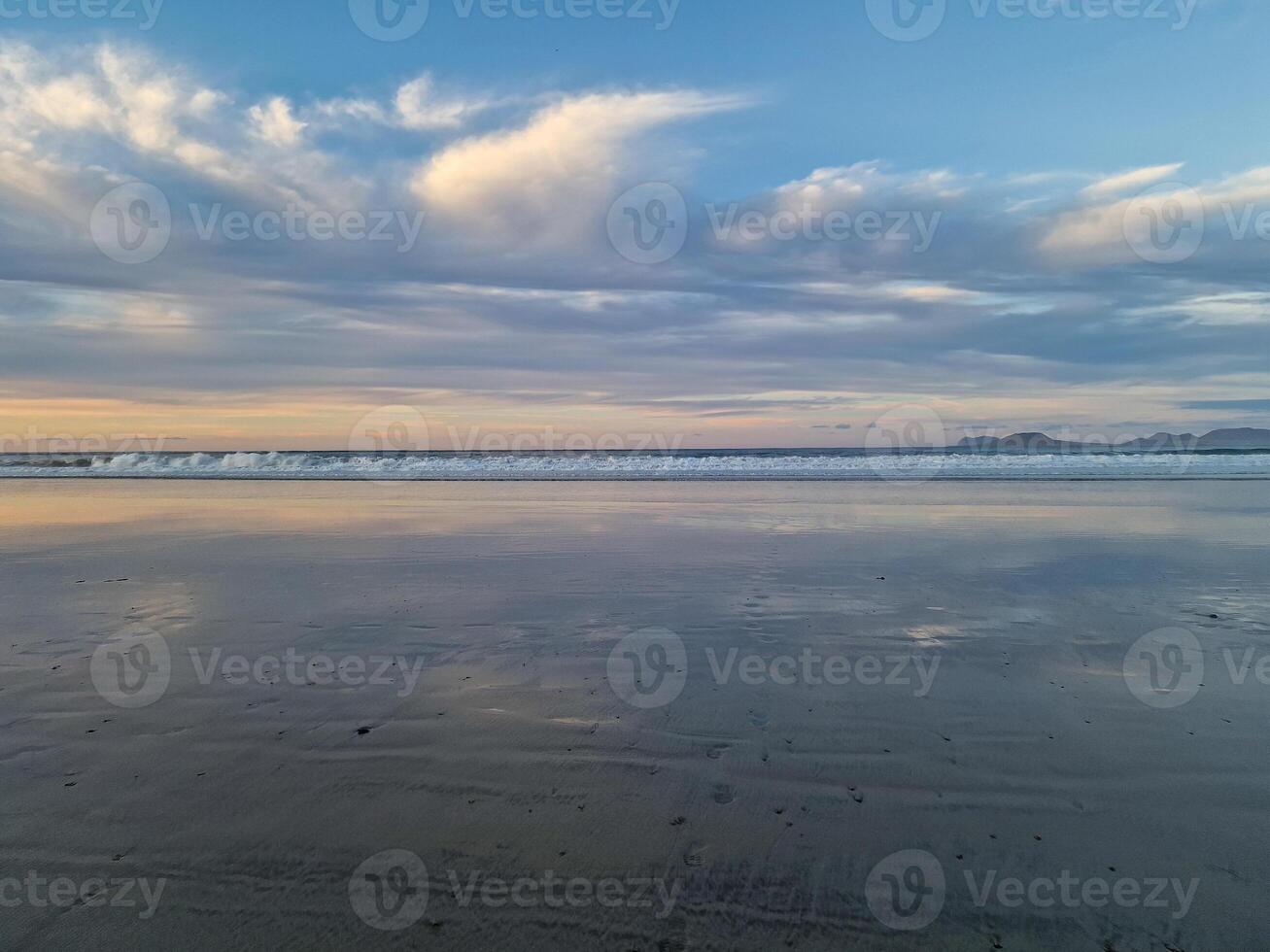 Sunset at Playa de Famara, Lanzarote, paints the sky with vibrant hues, casting a mesmerizing glow over the horizon. Breathtaking sight that captures the essence of tranquility and natural beauty. photo