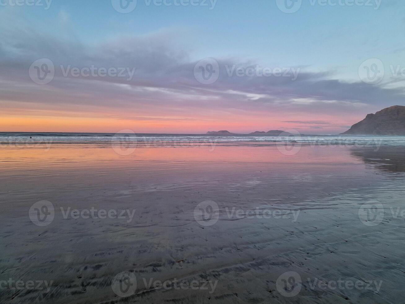 Sunset at Playa de Famara, Lanzarote, paints the sky with vibrant hues, casting a mesmerizing glow over the horizon. Breathtaking sight that captures the essence of tranquility and natural beauty. photo