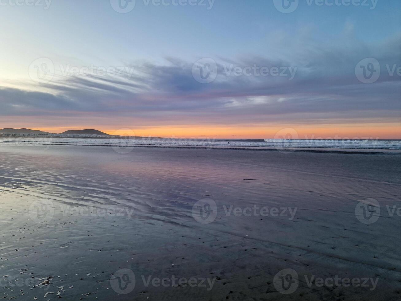 Sunset at Playa de Famara, Lanzarote, paints the sky with vibrant hues, casting a mesmerizing glow over the horizon. Breathtaking sight that captures the essence of tranquility and natural beauty. photo