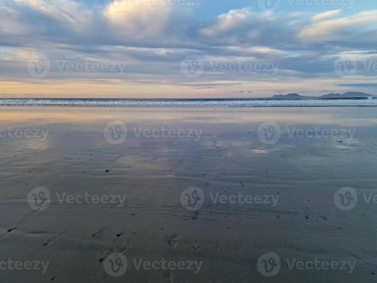 Sunset at Playa de Famara, Lanzarote, paints the sky with vibrant hues, casting a mesmerizing glow over the horizon. Breathtaking sight that captures the essence of tranquility and natural beauty. photo