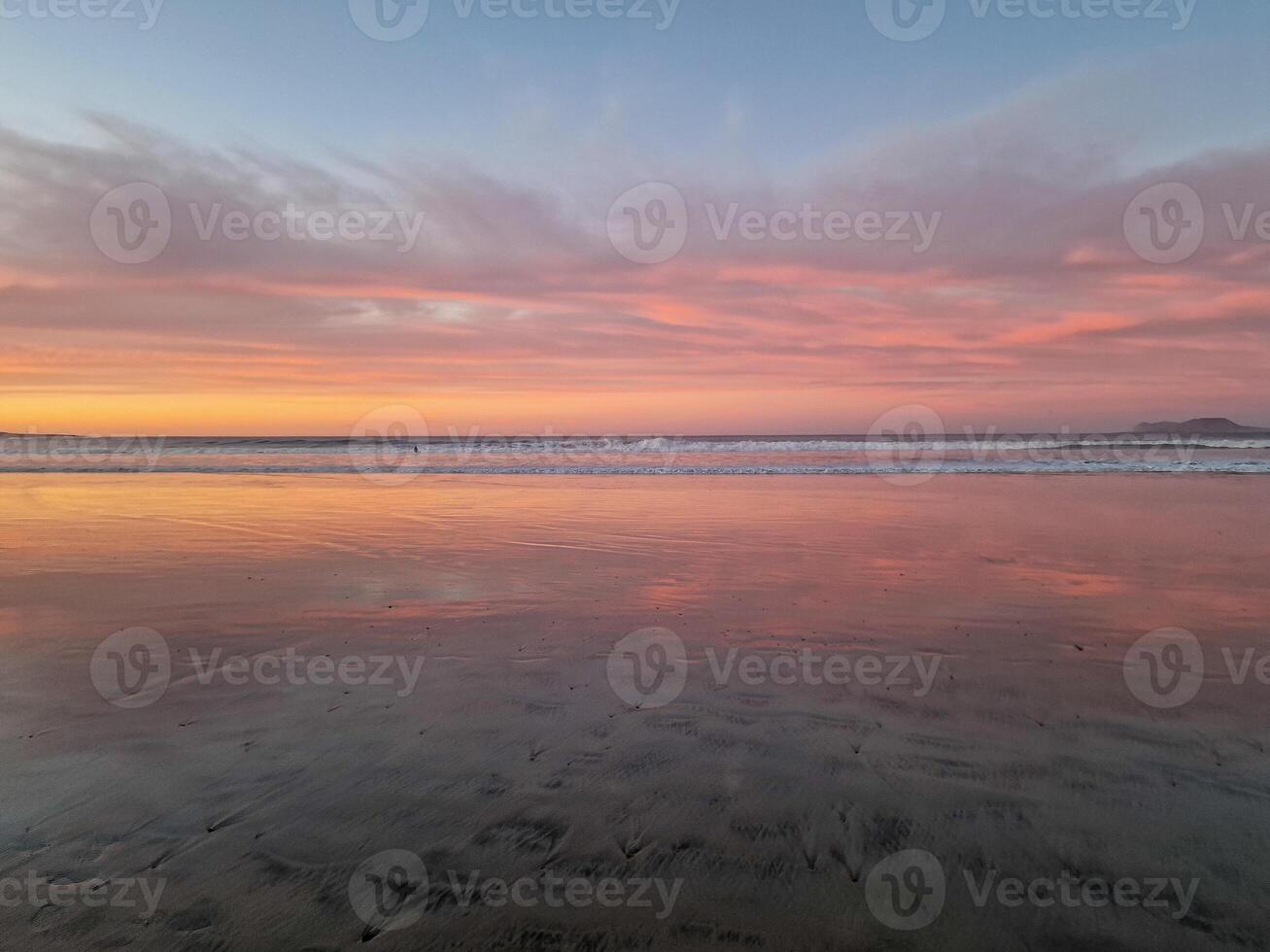 Sunset at Playa de Famara, Lanzarote, paints the sky with vibrant hues, casting a mesmerizing glow over the horizon. Breathtaking sight that captures the essence of tranquility and natural beauty. photo