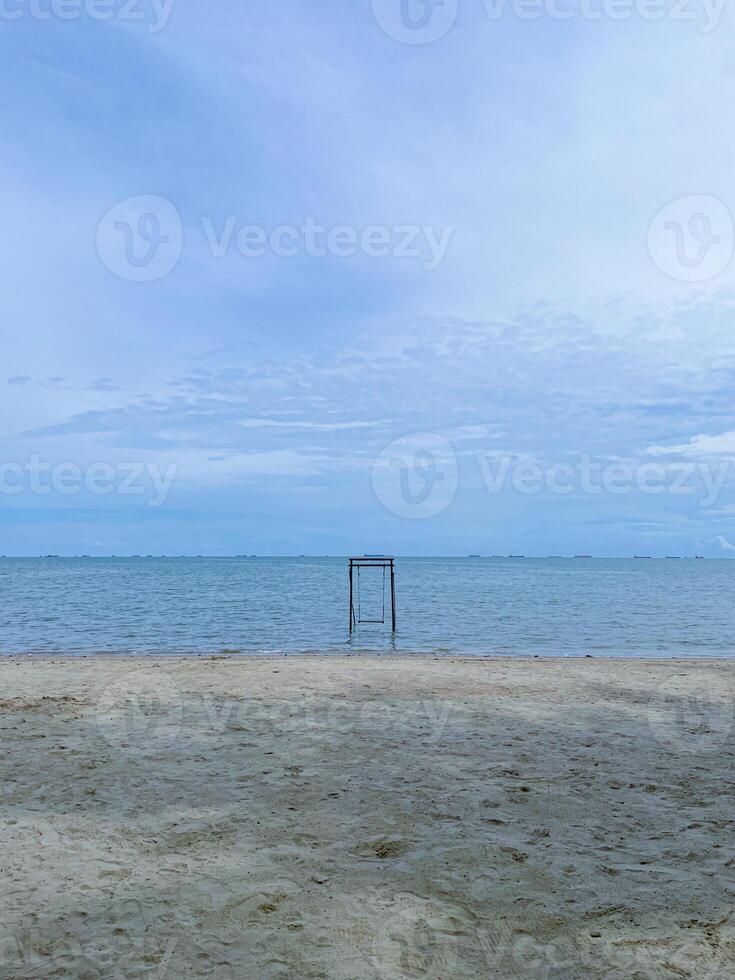 photo of a beach view with a cloudy sky and a swing in the middle of the beach