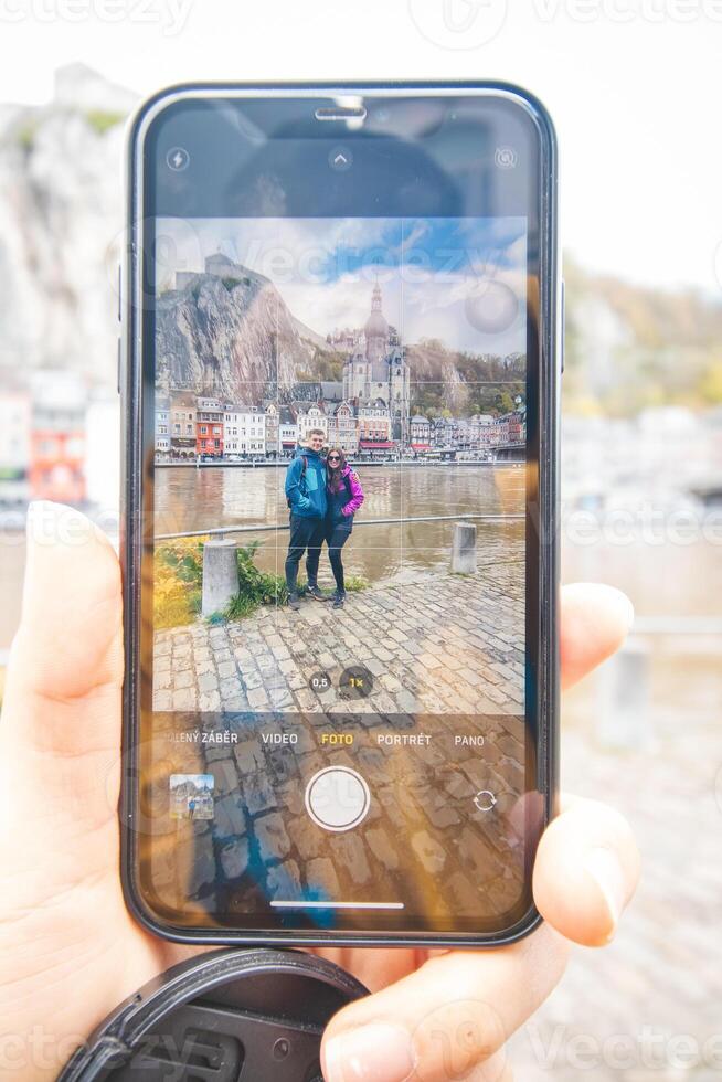 couple in love standing on the banks of the river La Meuse in front of the landmark town of Dinant, photographed with a mobile phone. Daylight photo