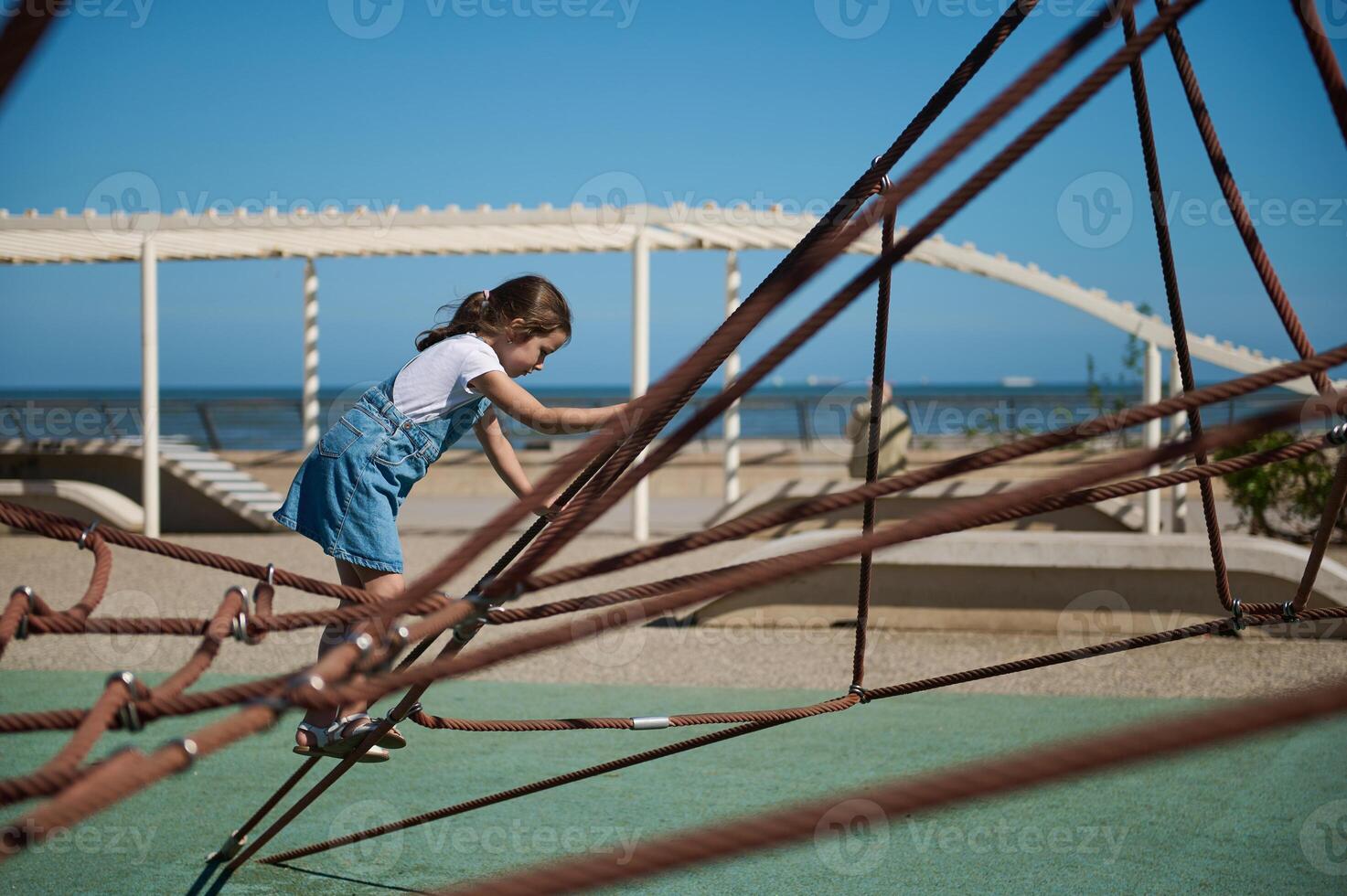 Adorable little girl climbing on a climbing net at the city playground on the embankment. photo