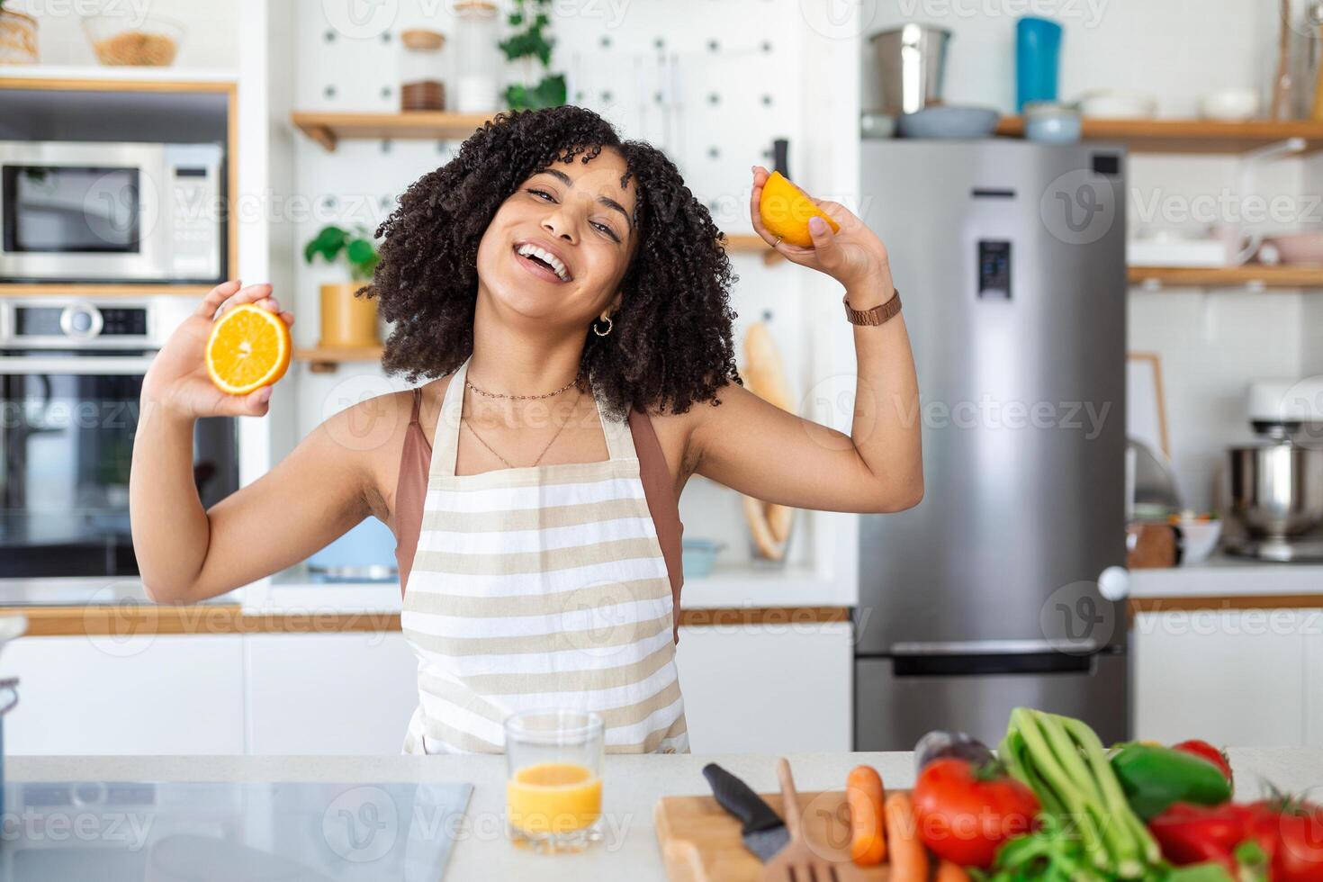 Beautiful young woman drinking fresh orange juice in kitchen. Healthy diet. Happy young woman with glass of juice and orange at table in kitchen. photo