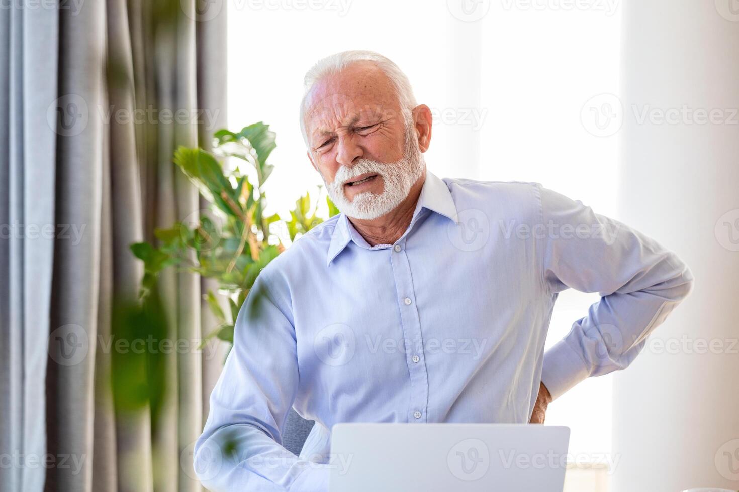 Senior businessman working sitting at desk suffers from lower back pain. Damage of intervertebral discs, spinal joints, compression of nerve roots caused by wrong posture and sedentary work photo