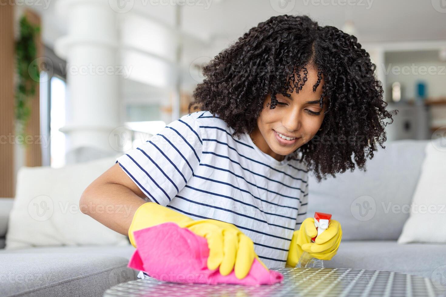 Young beautiful woman tidying up the living room and wiping the dining table surface with a cloth. photo