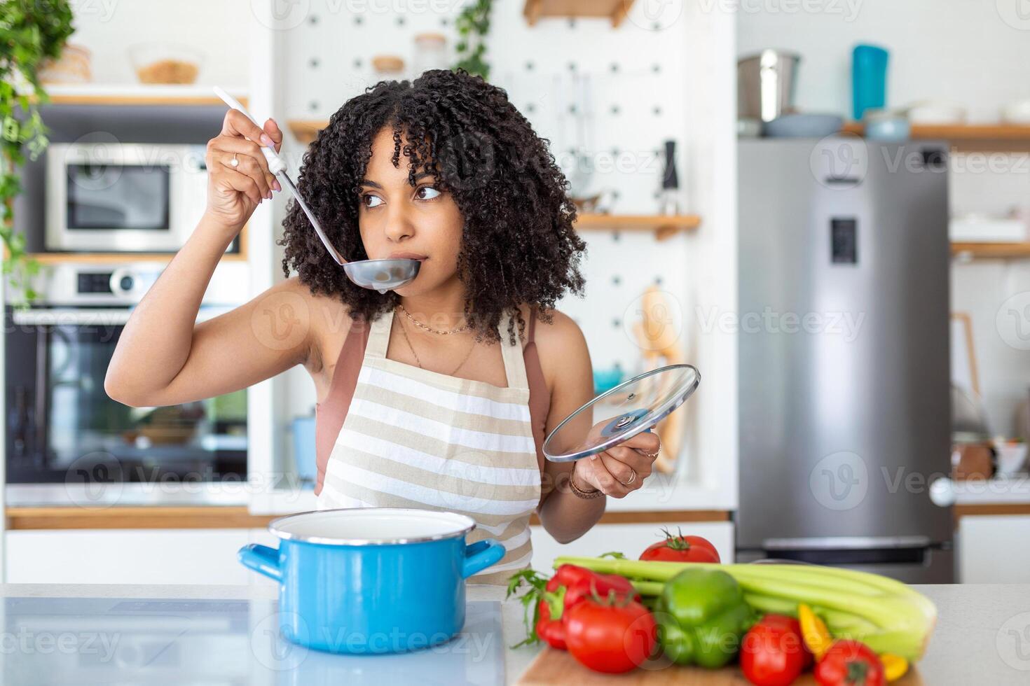 Happy Young Woman Cooking Tasting Dinner In A Pot Standing In Modern Kitchen At Home. Housewife Preparing Healthy Food Smiling . Household And Nutrition. Dieting Recipes Concept photo