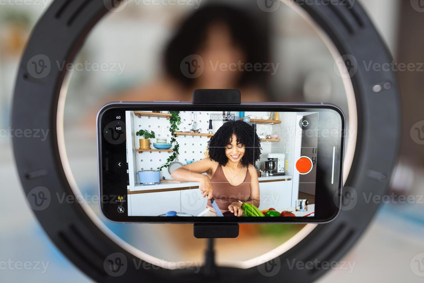 African American woman chef vlogger shoot cooking food vlog blog on smartphone at home kitchen. Young woman record recipe or tutorial on cellphone preparing healthy vegetarian dish. photo