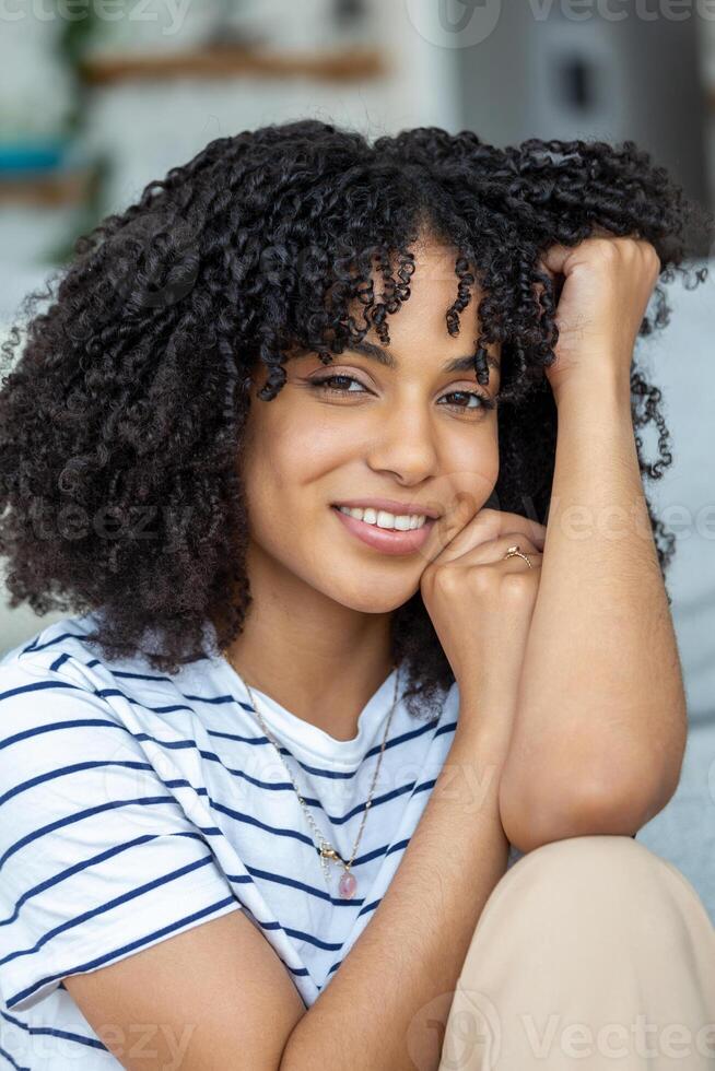Portrait of a beautiful woman smiling at home. African woman in casual looking at camera with copy space. Cheerful mixed race girl relaxing at home with big laugh. photo