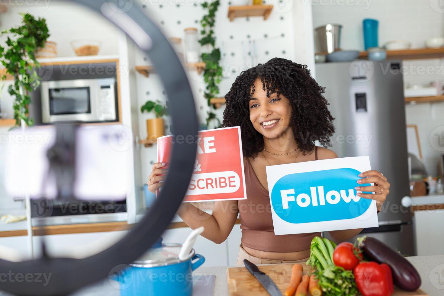 Young female blogger recording video while cooking in kitchen. Woman recording video in her home kitchen, asking online audience to like and subscribe to her channel, daily videos photo