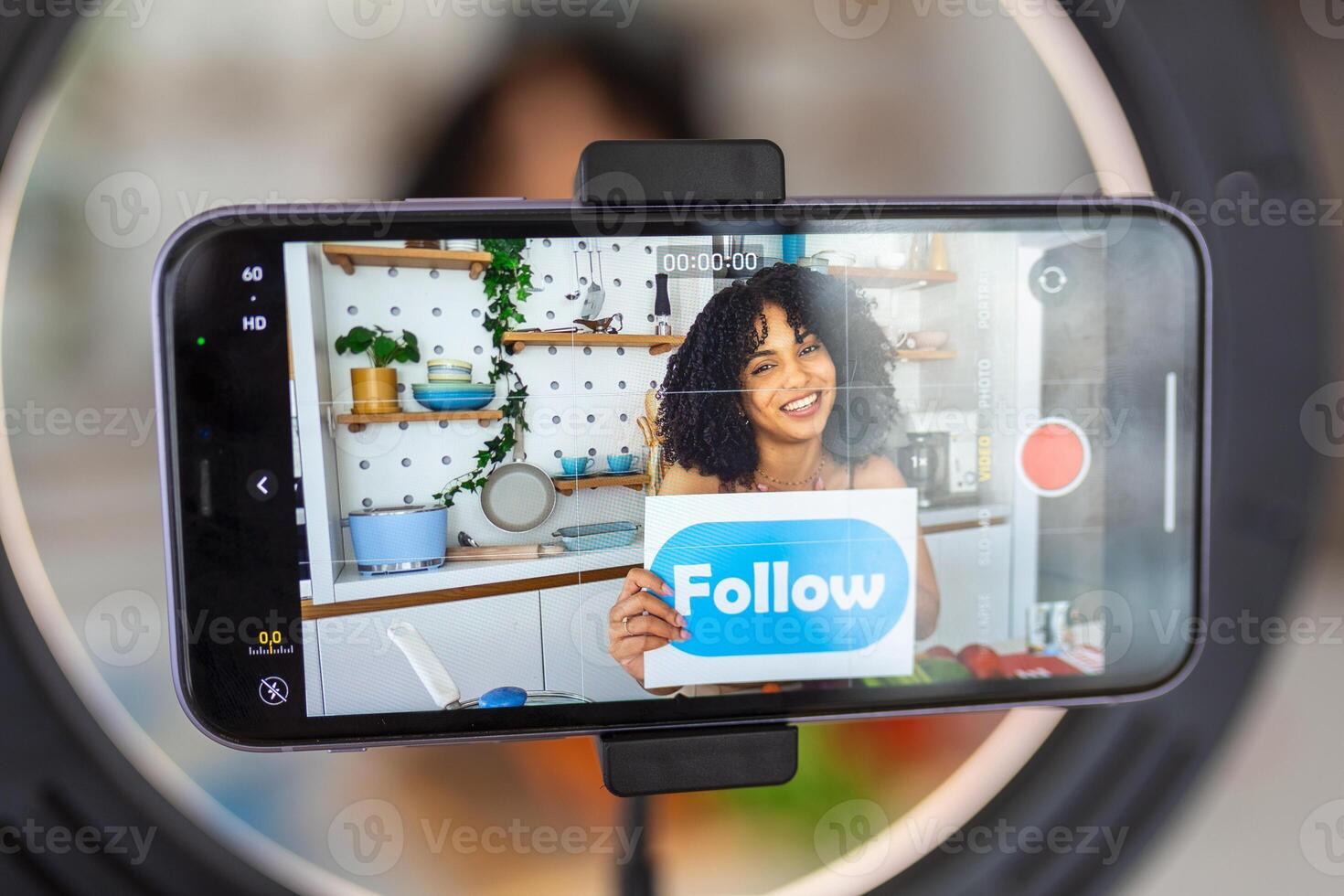 Happy african american woman vlogger broadcasting live video online while cooking food in kitchen at home holding follow sign photo