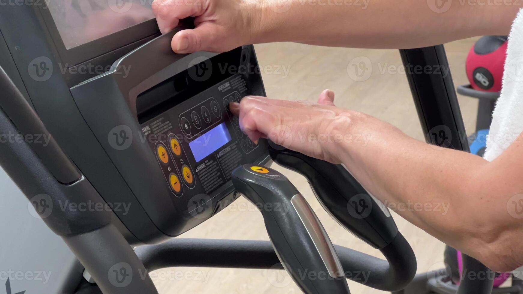 An elliptical cross-trainer is programmed for cardio training by a woman's hand. Hands of an elderly woman on the exercise machine. photo