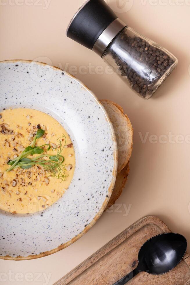 Plate of cheese cream soup with nuts and greens on beige background top view. photo