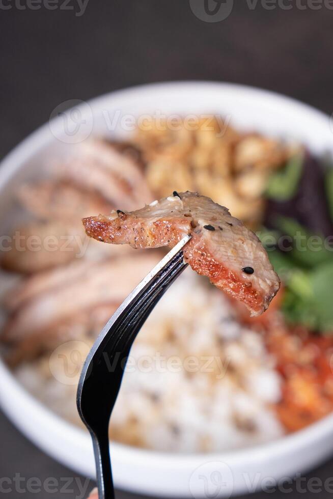 Meat on fork close-up on background of bowl with rice, veal and vegetables. photo
