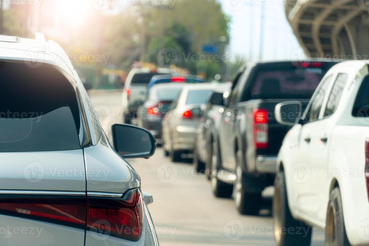 Rear side view of white car driving on the road. with other cars. Background blurred of bridge and trees under sky in the city. Cars lined up on the road in urgent traffic condition. photo