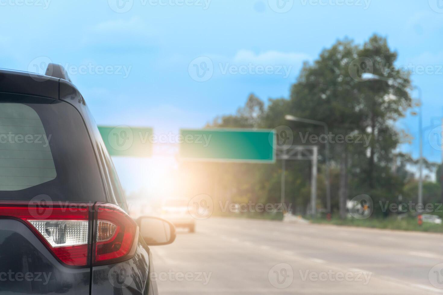 Rear side of a grey car on the road with other cars driving on the road. Sign borad green on top of road. Blurred background of trees under blue sky. photo