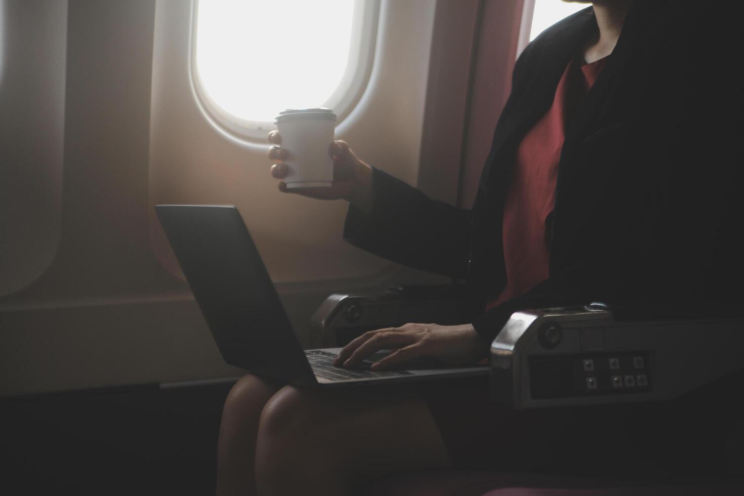 Blonde female tourist checking incoming notification on smartphone sitting on seat of airplane with netbook.Young businesswoman share media from telephone on laptop computer during plane flight photo