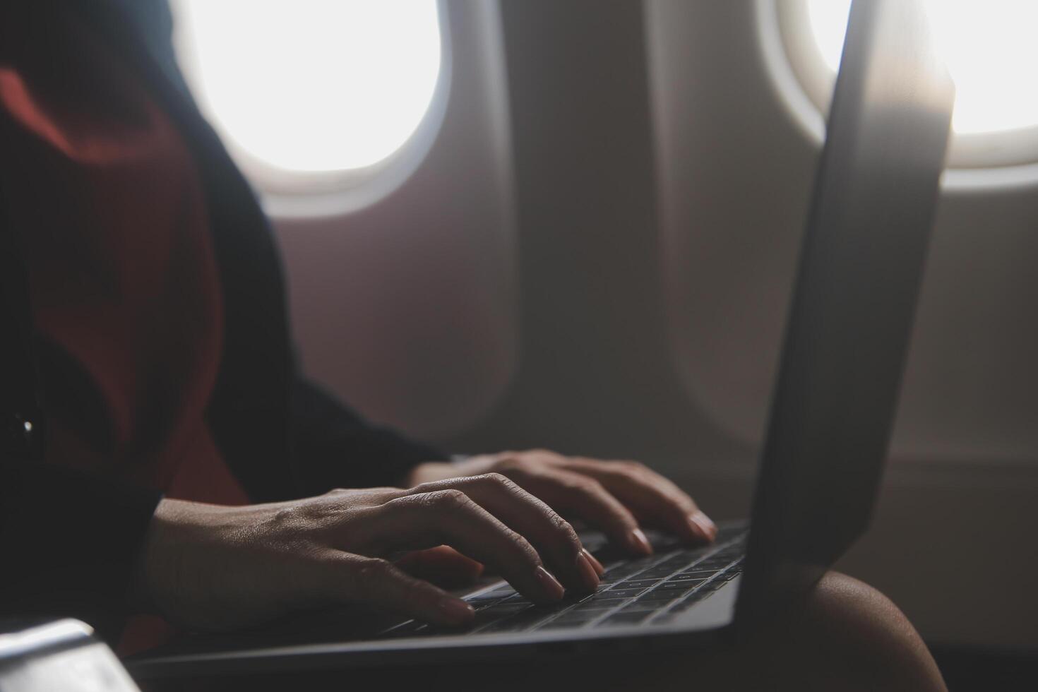 Blonde female tourist checking incoming notification on smartphone sitting on seat of airplane with netbook.Young businesswoman share media from telephone on laptop computer during plane flight photo