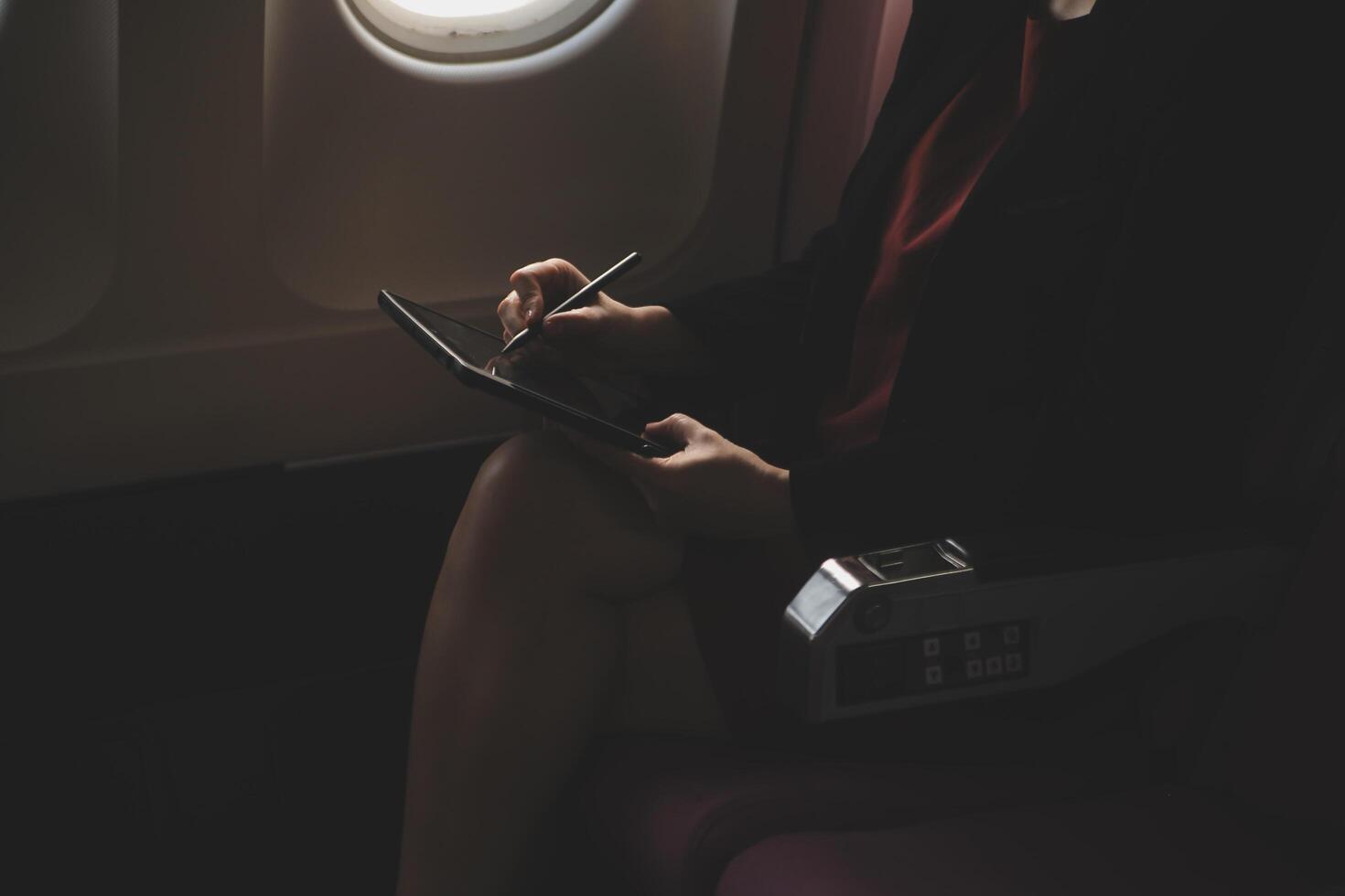 Blonde female tourist checking incoming notification on smartphone sitting on seat of airplane with netbook.Young businesswoman share media from telephone on laptop computer during plane flight photo