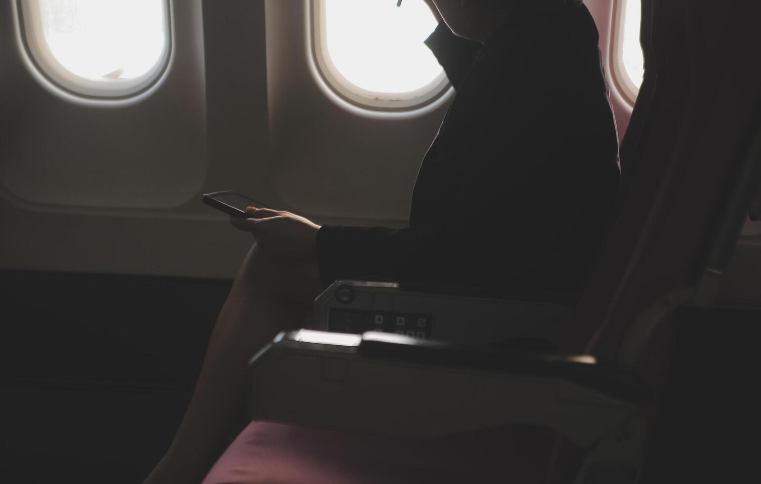 Blonde female tourist checking incoming notification on smartphone sitting on seat of airplane with netbook.Young businesswoman share media from telephone on laptop computer during plane flight photo