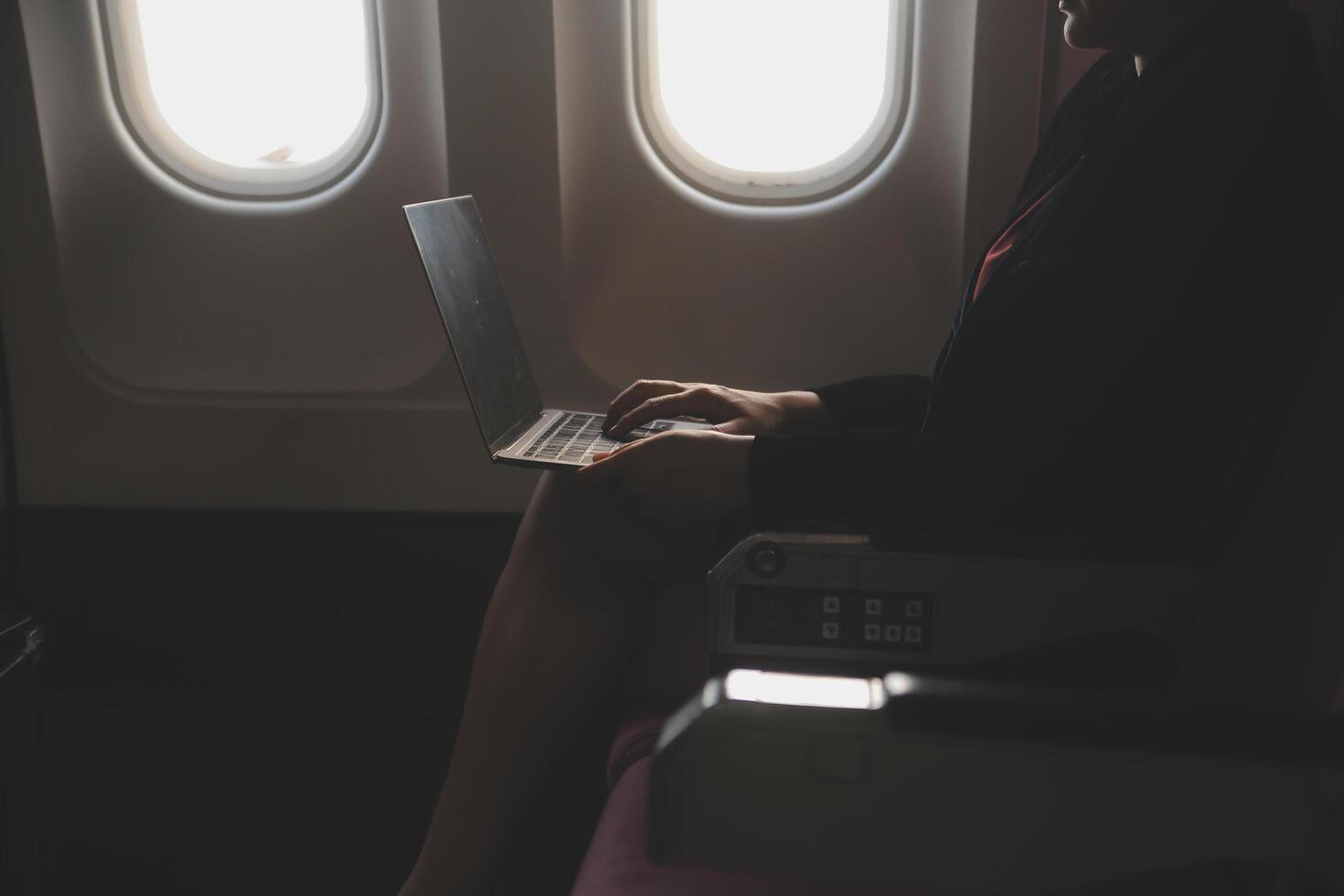 Blonde female tourist checking incoming notification on smartphone sitting on seat of airplane with netbook.Young businesswoman share media from telephone on laptop computer during plane flight photo