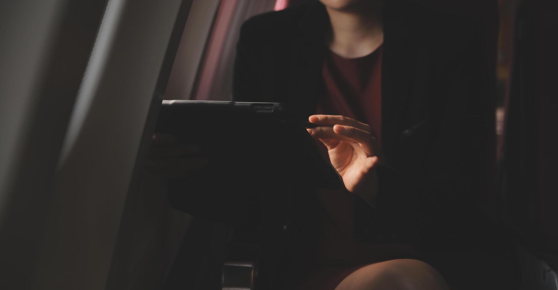 Blonde female tourist checking incoming notification on smartphone sitting on seat of airplane with netbook.Young businesswoman share media from telephone on laptop computer during plane flight photo