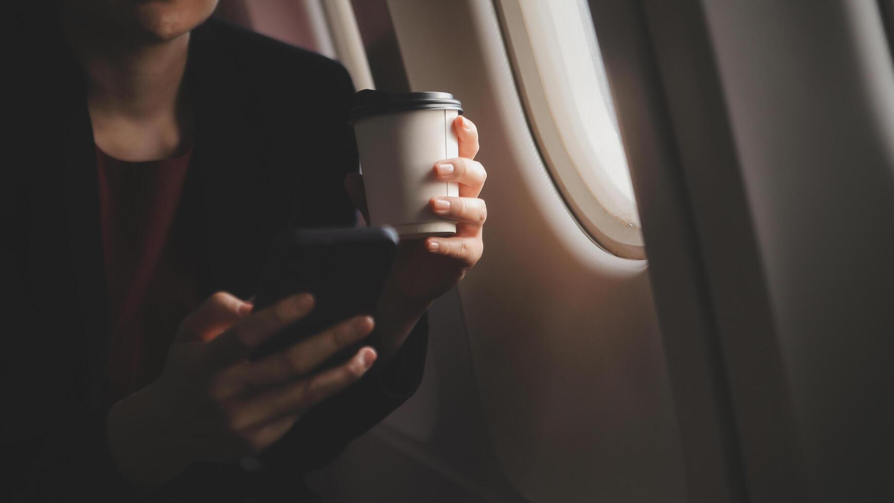 Blonde female tourist checking incoming notification on smartphone sitting on seat of airplane with netbook.Young businesswoman share media from telephone on laptop computer during plane flight photo