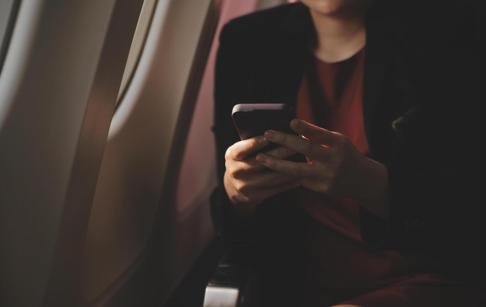 Blonde female tourist checking incoming notification on smartphone sitting on seat of airplane with netbook.Young businesswoman share media from telephone on laptop computer during plane flight photo