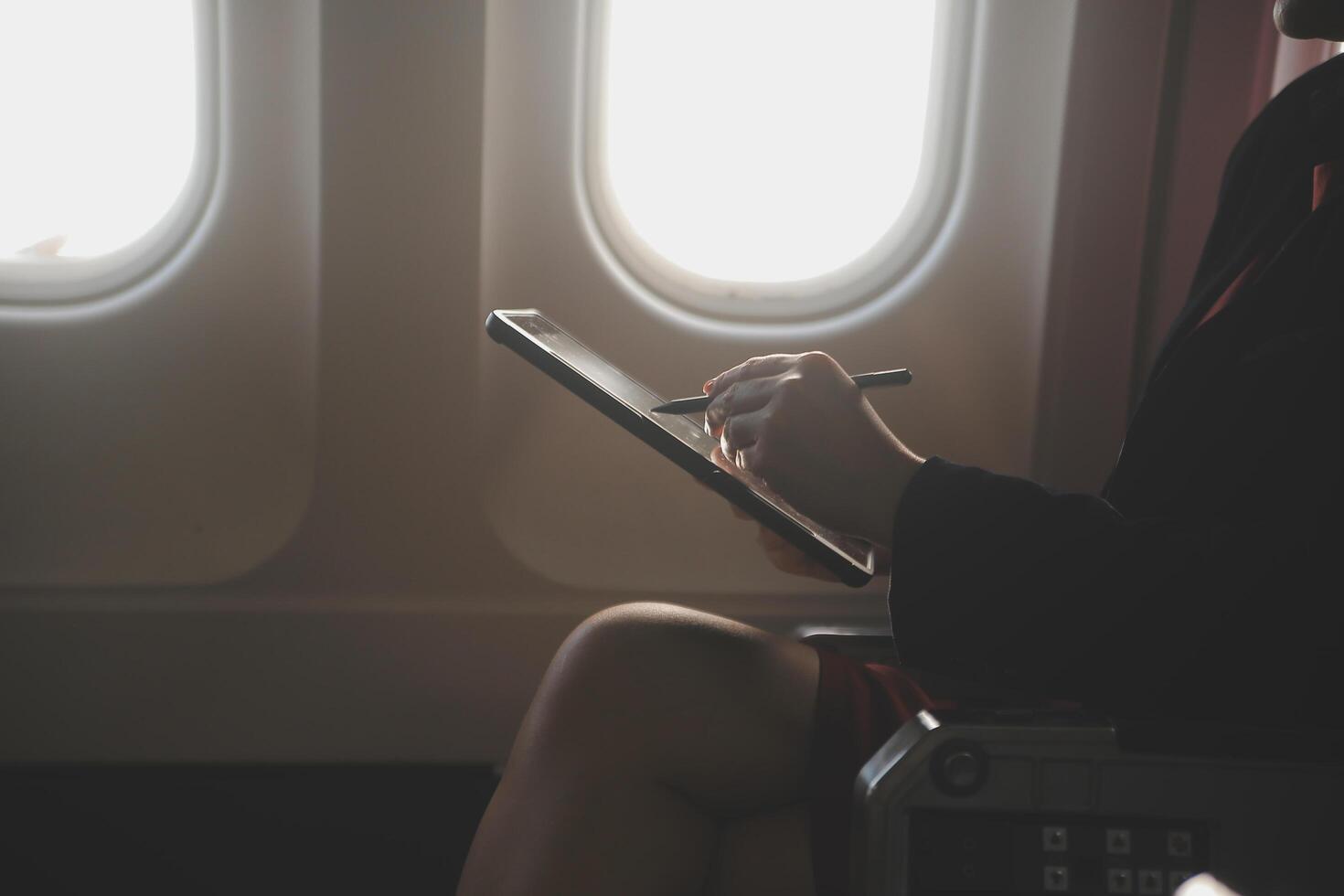 Blonde female tourist checking incoming notification on smartphone sitting on seat of airplane with netbook.Young businesswoman share media from telephone on laptop computer during plane flight photo