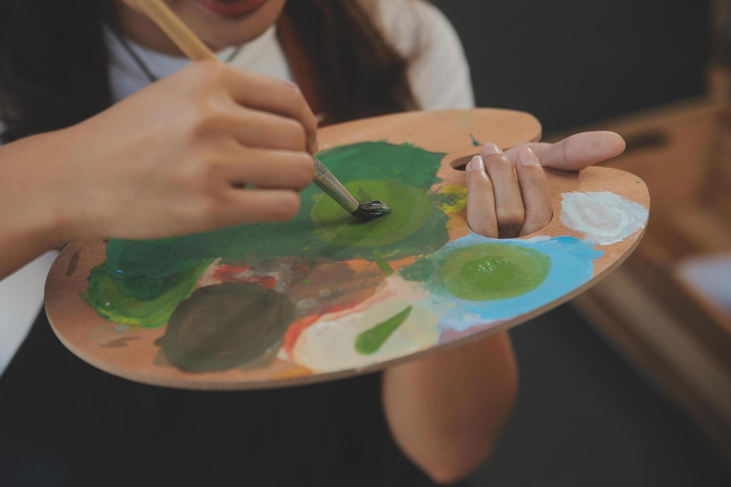 Cropped image of female artist standing in front of an easel and dipping brush into color palette photo