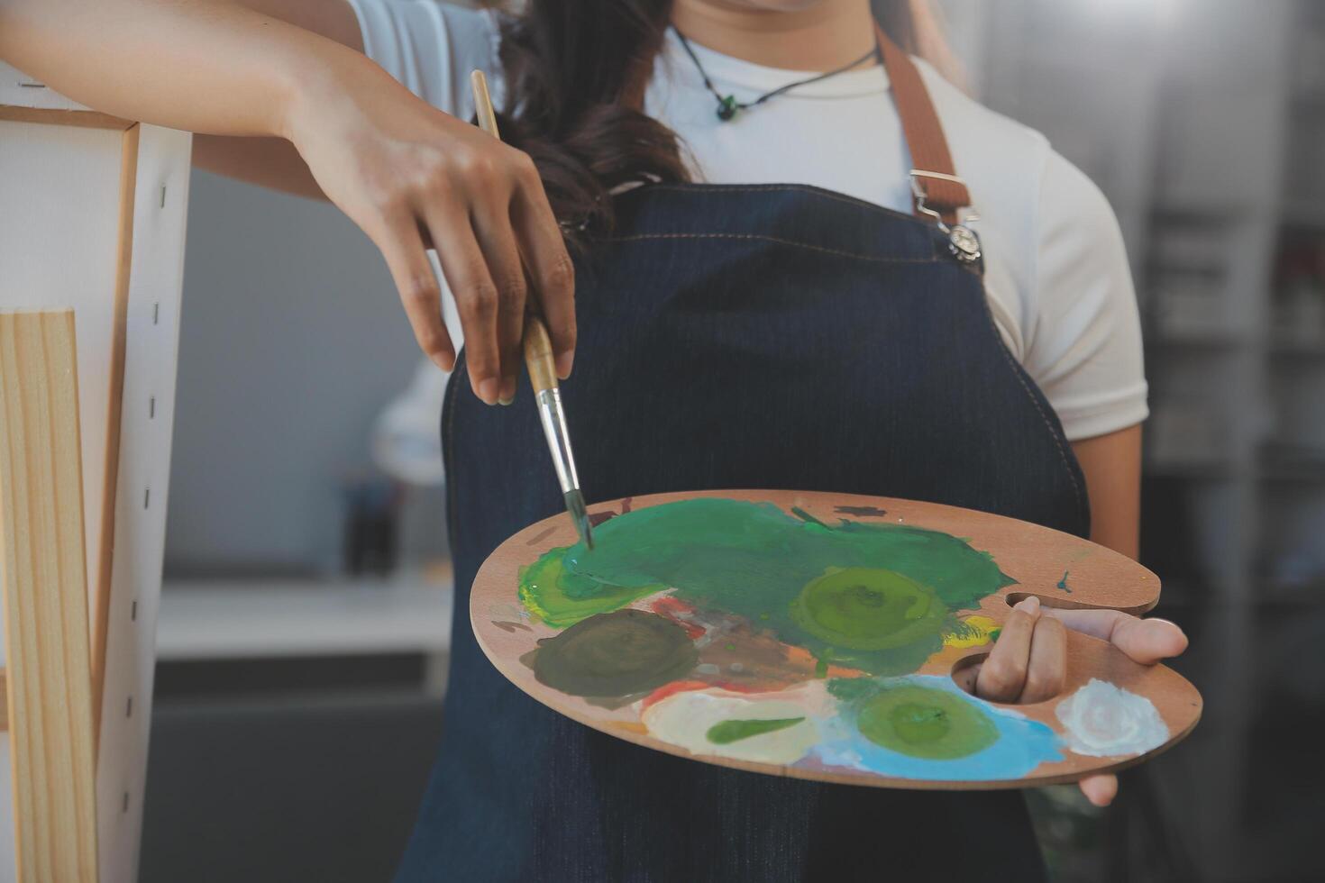 Cropped image of female artist standing in front of an easel and dipping brush into color palette photo
