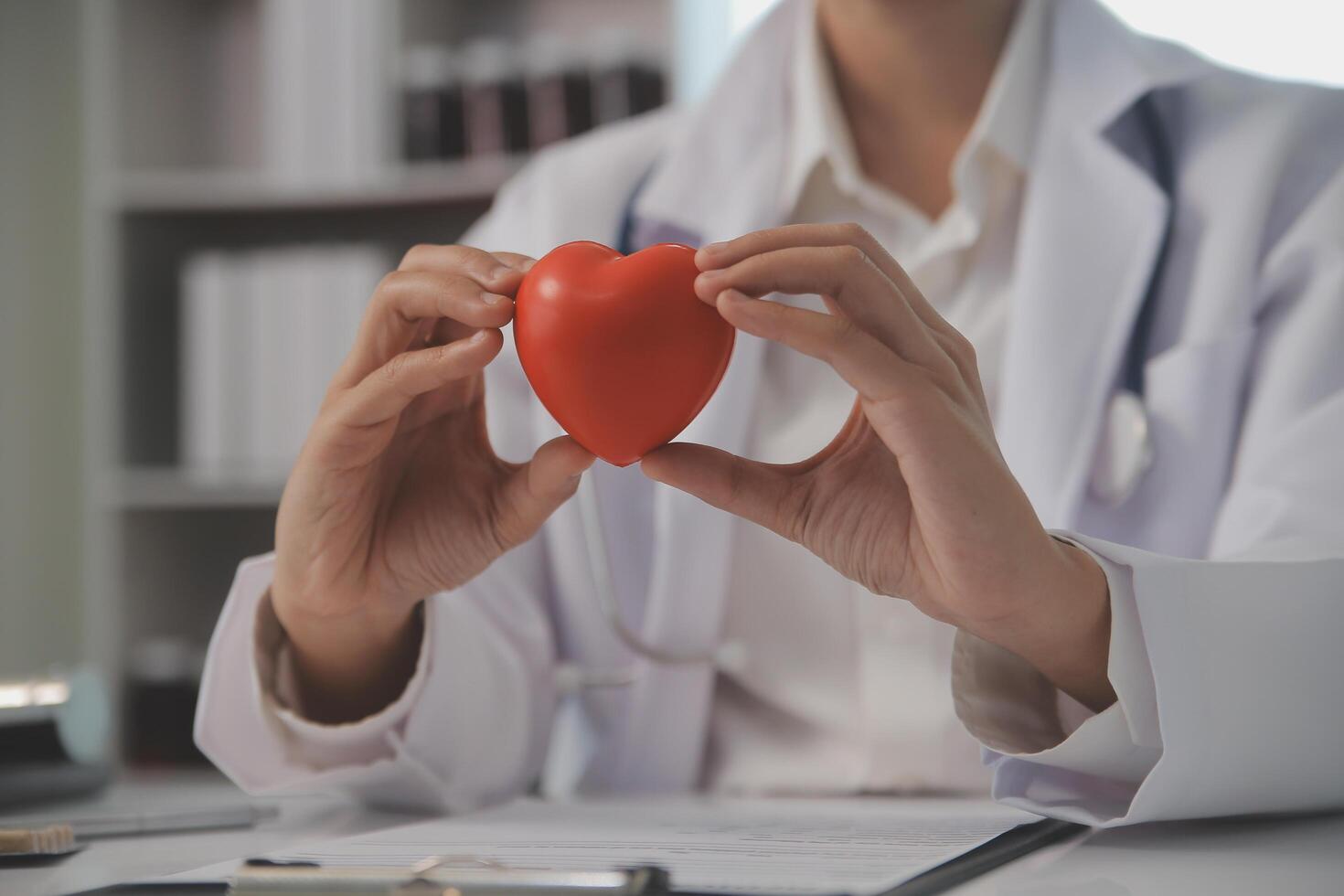 Hands of doctor woman holding red heart, showing symbol of love, human support to patient, promoting medical insurance, early checkup for healthcare, cardiologist help. Close up of object photo