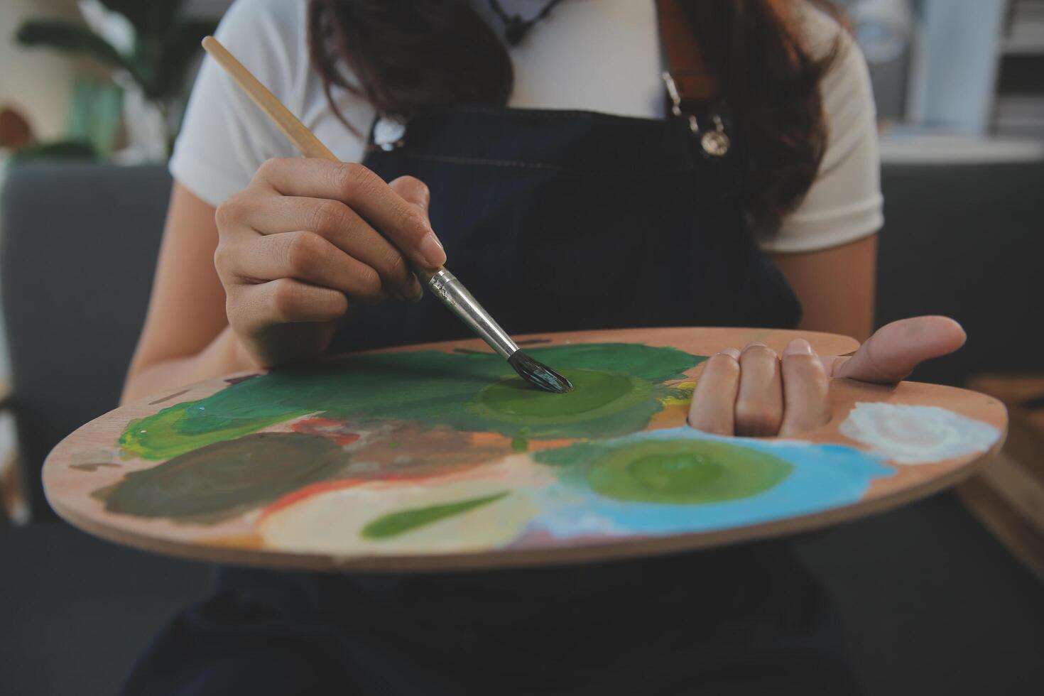 Cropped image of female artist standing in front of an easel and dipping brush into color palette photo