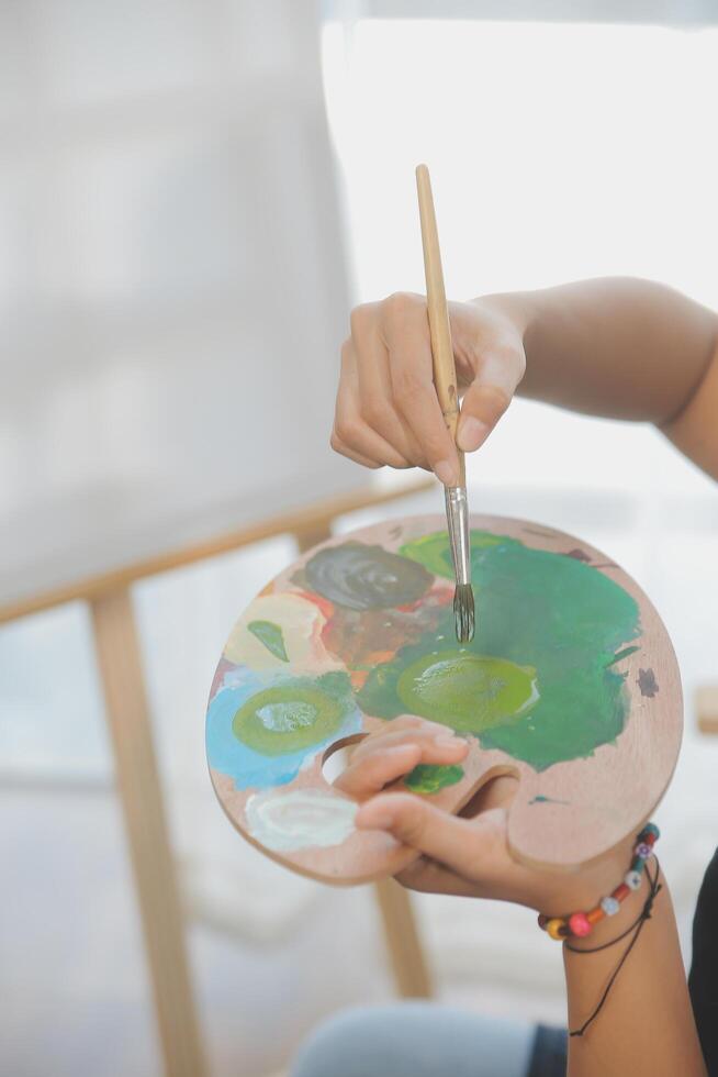 Cropped image of female artist standing in front of an easel and dipping brush into color palette photo