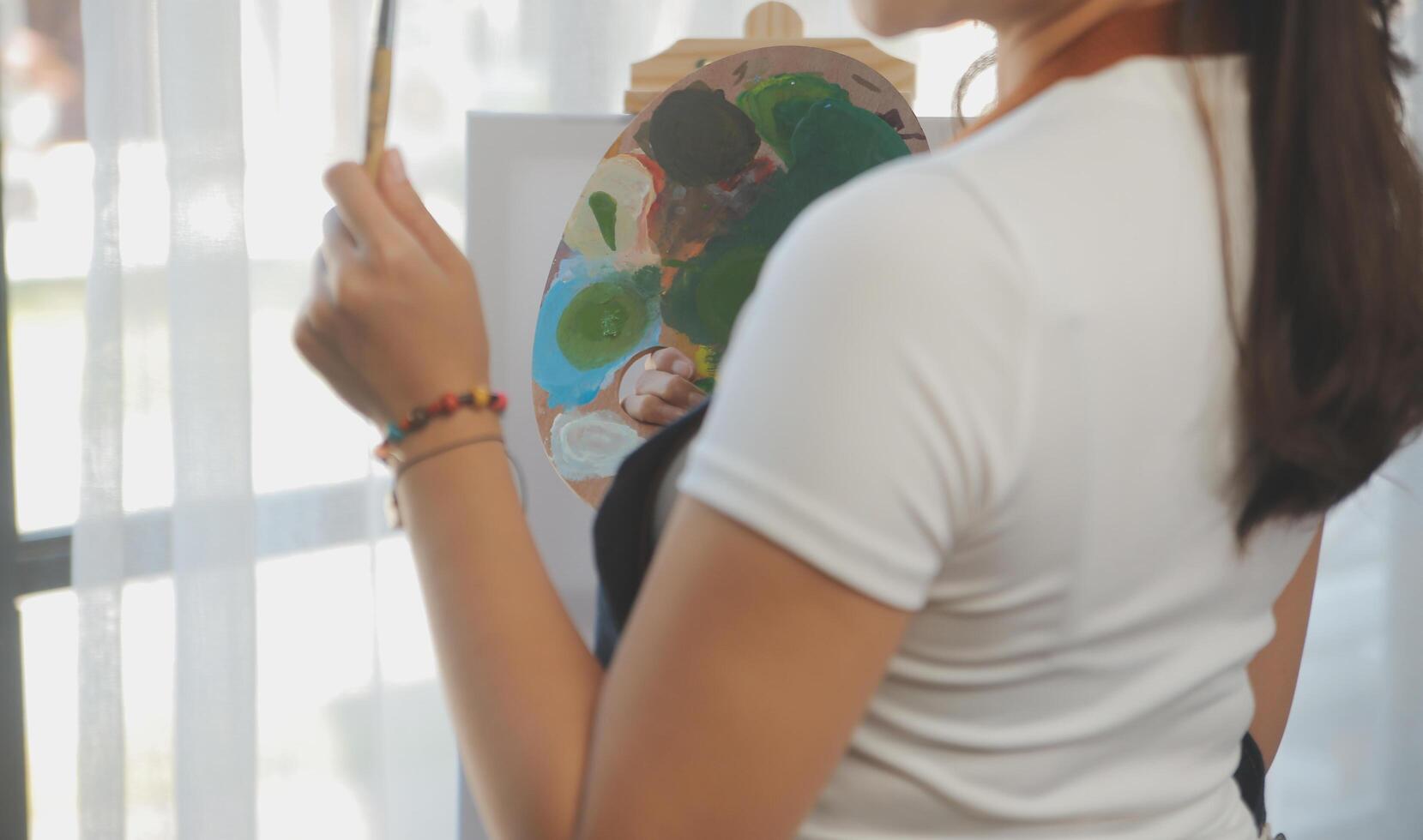 Cropped image of female artist standing in front of an easel and dipping brush into color palette photo
