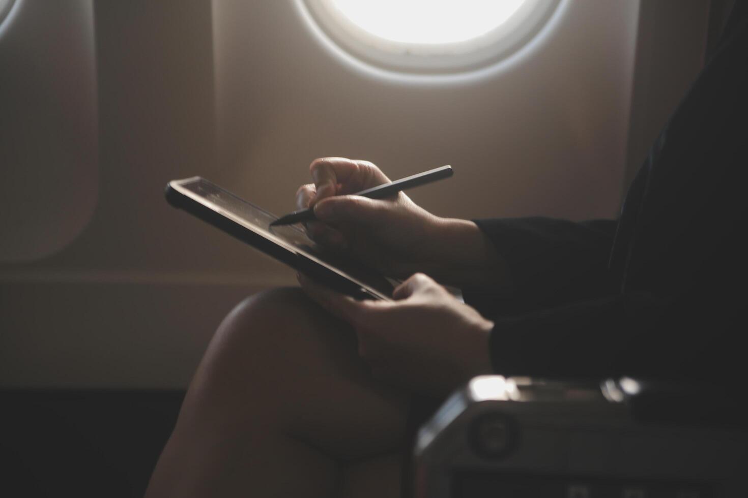 Blonde female tourist checking incoming notification on smartphone sitting on seat of airplane with netbook.Young businesswoman share media from telephone on laptop computer during plane flight photo