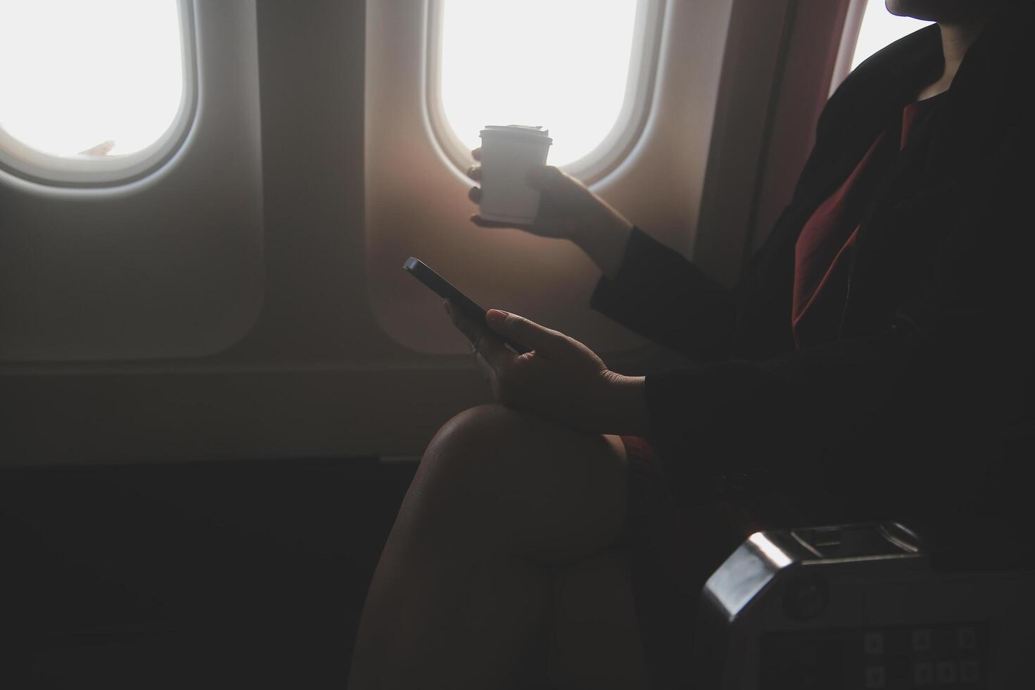Blonde female tourist checking incoming notification on smartphone sitting on seat of airplane with netbook.Young businesswoman share media from telephone on laptop computer during plane flight photo