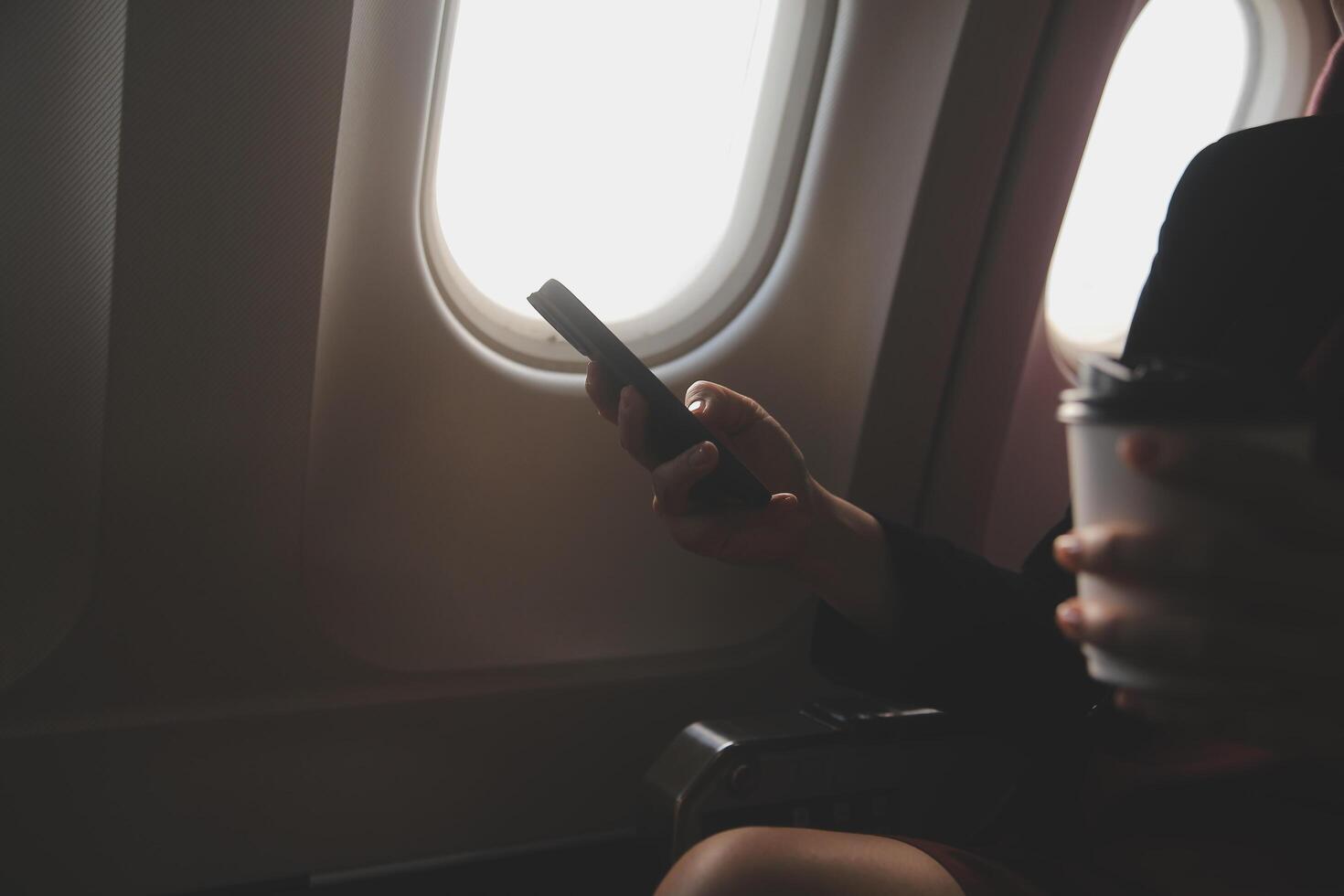 Blonde female tourist checking incoming notification on smartphone sitting on seat of airplane with netbook.Young businesswoman share media from telephone on laptop computer during plane flight photo