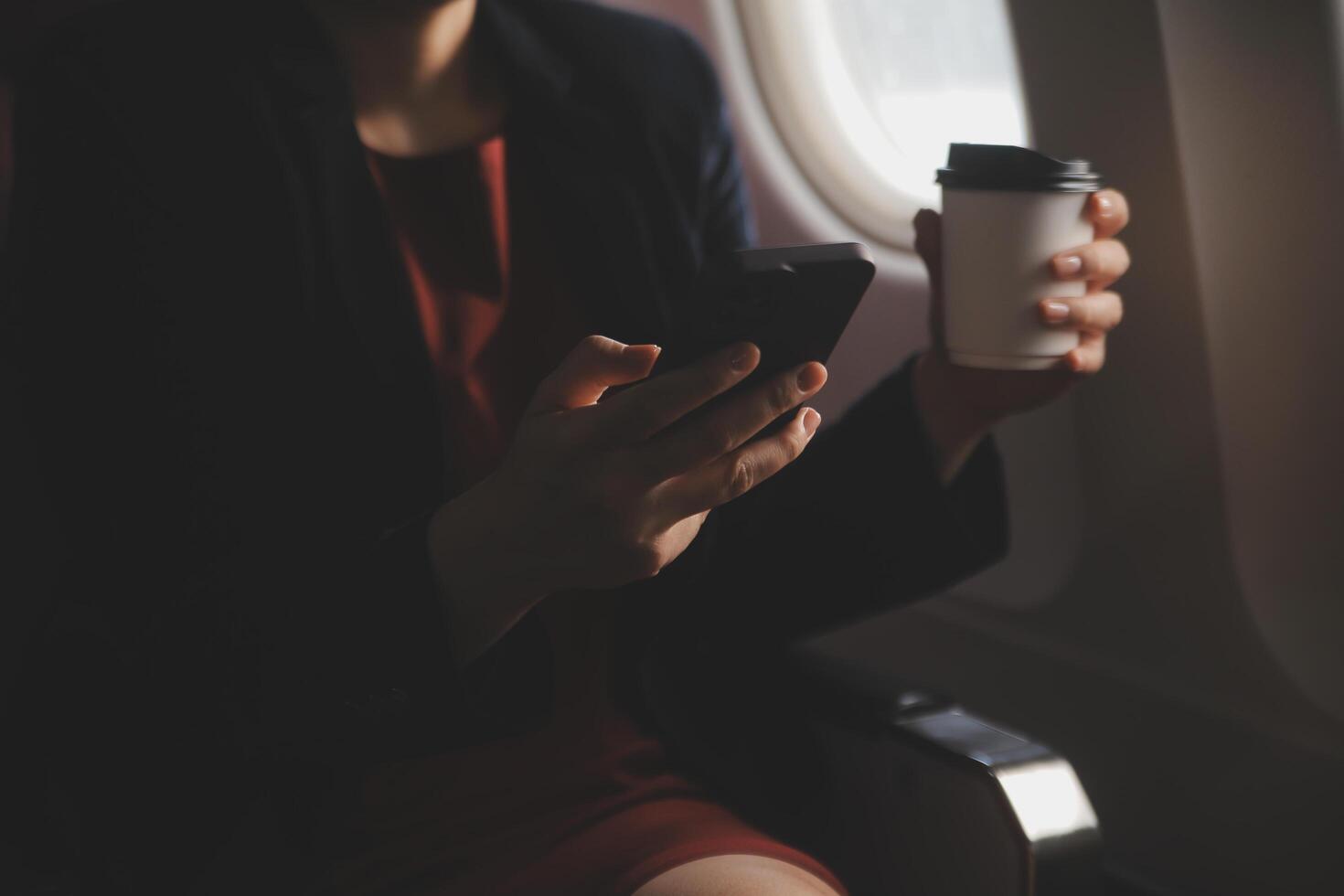 Blonde female tourist checking incoming notification on smartphone sitting on seat of airplane with netbook.Young businesswoman share media from telephone on laptop computer during plane flight photo