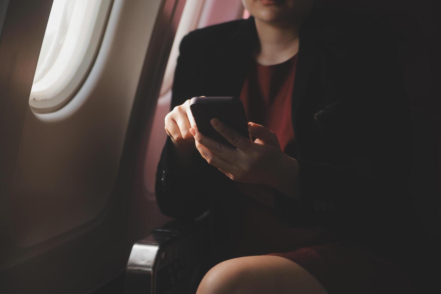 Blonde female tourist checking incoming notification on smartphone sitting on seat of airplane with netbook.Young businesswoman share media from telephone on laptop computer during plane flight photo